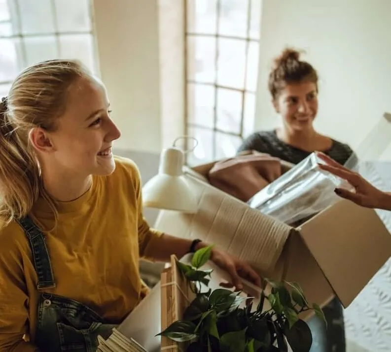 To unge kvinner pakker ut flytteesker i en lys leilighet